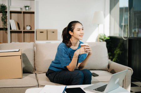 Foto de Asiática mujer de negocios utilizando el ordenador portátil con una sonrisa mientras está sentado en el sofá en casa oficina - Imagen libre de derechos