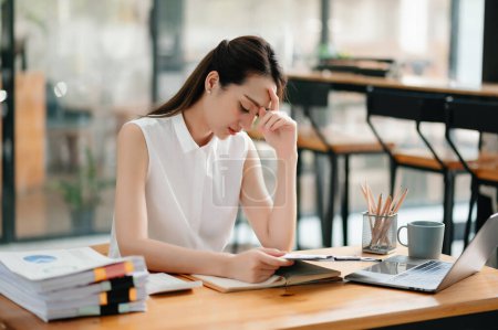 Foto de Mujer asiática sensación migraña cabeza strain.Overworked financiero mujer de negocios mientras trabajaba en el ordenador portátil en la oficina. - Imagen libre de derechos