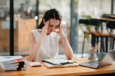 Téléchargez les photos : Femme asiatique se sentant migraine tête tendue.Overworked femme d'affaires financière tout en travaillant sur ordinateur portable au bureau. - en image libre de droit
