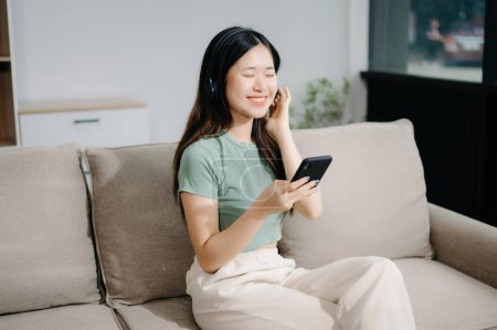 Téléchargez les photos : Jeune femme asiatique se détendre sur un canapé confortable à la maison textos sur smartphone - en image libre de droit