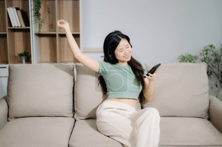 Foto de Joven asiático mujer relajarse en cómodo sofá en casa mensajes de texto en el teléfono inteligente - Imagen libre de derechos