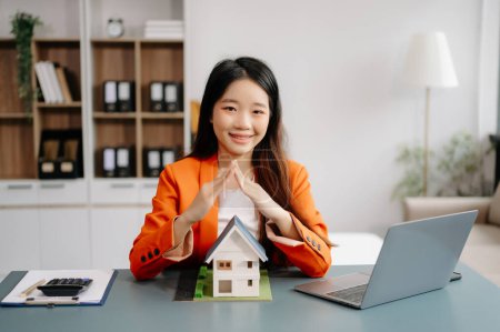 Téléchargez les photos : Femme agent immobilier est utiliser les mains pour protéger le toit rouge pour le concept d'investissement immobilier sur le commerce de la maison, achat au bureau au bureau - en image libre de droit
