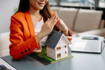 Photo for Female real estate agent is use hands to protect red roof for the concept of real estate investment about house trading, purchase at desk in office - Royalty Free Image