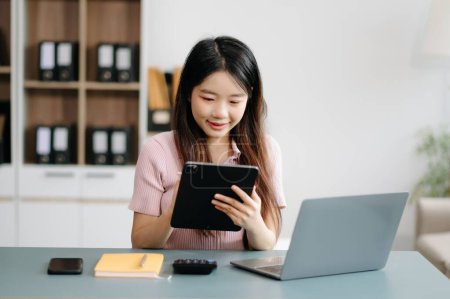 Foto de Mujer asiática sentada en un escritorio usando una computadora portátil. Navegar por las finanzas y el marketing con tecnología en la oficina - Imagen libre de derechos