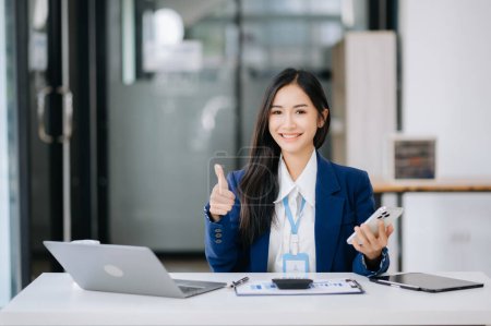 Foto de Joven mujer de negocios asiática mostrando los pulgares hacia arriba mientras trabaja en la oficina - Imagen libre de derechos