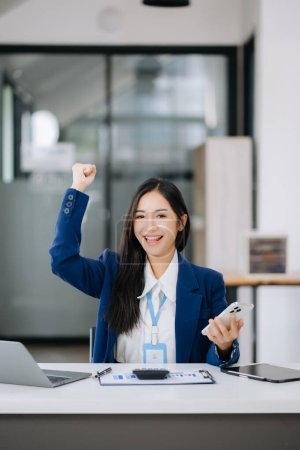 Téléchargez les photos : Asiatique femme d'affaires heureux avec le travail sur ordinateur portable au bureau - en image libre de droit