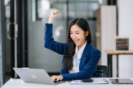 Téléchargez les photos : Asiatique femme d'affaires heureux avec le travail sur ordinateur portable au bureau - en image libre de droit