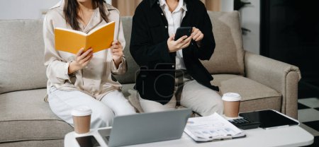 Photo for Two Young  business workers talking using laptop and smartphone on sofa at the office - Royalty Free Image