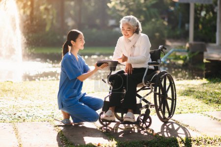 Photo for Elderly asian senior woman on wheelchair with careful caregiver in garden - Royalty Free Image