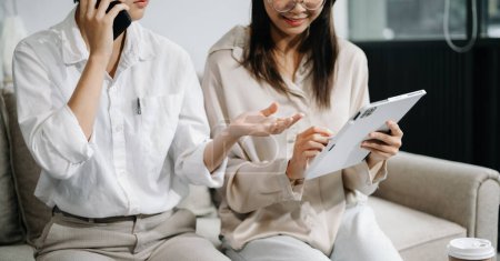 Téléchargez les photos : Deux femmes d'affaires asiatiques discutent de la stratégie de travail et de planification du projet d'investissement avec tablette sur canapé dans un bureau moderne - en image libre de droit