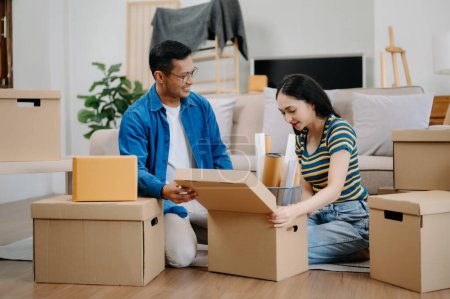 Téléchargez les photos : Jeune couple avec de grandes boîtes emménageant dans une nouvelle maison. Asiatique homme et femme aider à soulever des boîtes sur le canapé pour la nouvelle maison, Déménagement concept - en image libre de droit