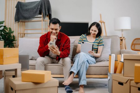 Téléchargez les photos : Asiatique jeune couple attrayant homme et femme utiliser smartphone et tablette pour les meubles de magasinage en ligne pour décorer nouvelle maison - en image libre de droit