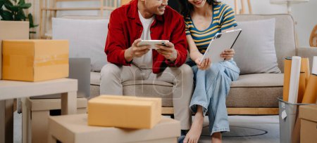 Foto de Asiático joven atractivo pareja hombre y mujer uso de teléfono inteligente y tableta para comprar muebles en línea para decorar nueva casa - Imagen libre de derechos