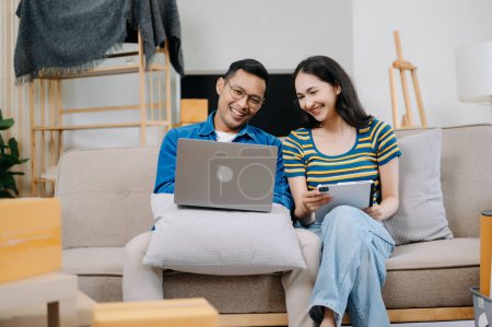 Téléchargez les photos : Asiatique jeune couple attrayant homme et femme utiliser ordinateur portable et tablette pour les meubles de magasinage en ligne pour décorer nouvelle maison - en image libre de droit