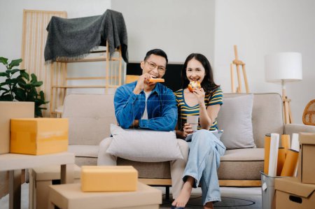 Photo for Happy asian young attractive couple man and woman having lunch with big boxes moving into a new house - Royalty Free Image