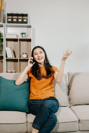Foto de Mujer asiática feliz usando el teléfono inteligente en el sofá en casa - Imagen libre de derechos