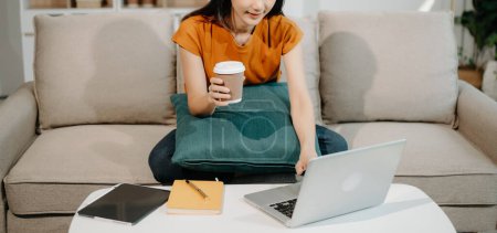 Foto de Mujer asiática sentada en un sofá usando una computadora portátil, Navegando Finanzas y Marketing con Tecnología en la oficina en casa - Imagen libre de derechos