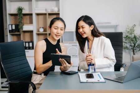 Téléchargez les photos : Deux femmes d'affaires asiatiques discutent du projet d'investissement, de la stratégie de travail et de planification avec tablette et ordinateur portable dans un bureau moderne - en image libre de droit