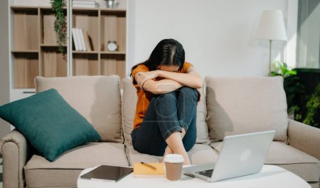 Téléchargez les photos : Asiatique femme fatigué et trop penser de travailler avec ordinateur portable sur canapé au bureau à la maison - en image libre de droit