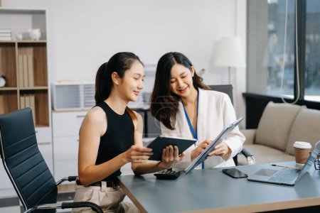 Foto de Dos empresarias asiáticas discuten el proyecto de inversión, la estrategia de trabajo y planificación con tableta y computadora portátil en la oficina moderna - Imagen libre de derechos