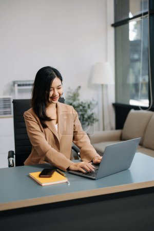Téléchargez les photos : Belle femme d'affaires asiatique utilisant smartphone et ordinateur portable à la table dans le bureau moderne - en image libre de droit