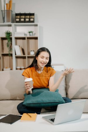 Téléchargez les photos : Femme asiatique assise sur un canapé à l'aide d'un ordinateur portable, Naviguer dans les finances et le marketing avec la technologie au bureau à domicile - en image libre de droit