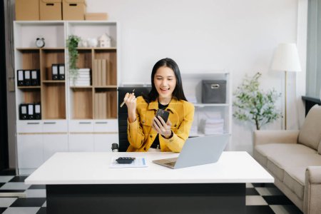 Téléchargez les photos : Asiatique femme d'affaires heureuse, tenant smartphone au bureau - en image libre de droit