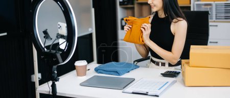 Foto de Concepto de blogger de moda, Mujer joven asiática vendiendo ropa en streaming de video. Puesta en marcha de pequeñas empresas PYME, utilizando smartphone, recepción y facturación en la oficina - Imagen libre de derechos