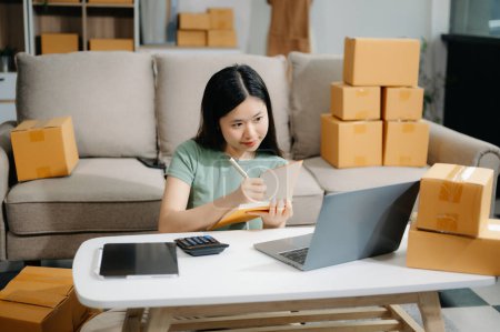 Photo for Startup small business SME, Entrepreneur owner woman using laptop computer taking receive and checking online purchase shopping order to preparing pack product box. - Royalty Free Image