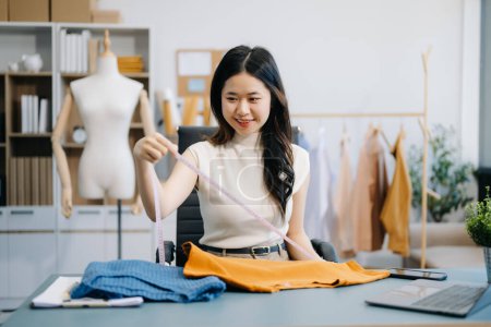 Photo for Asian tailor woman working on clothes in tailoring atelier. beautiful young female fashion designer smile after success in modern studio - Royalty Free Image