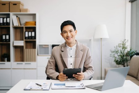 Foto de Hombre de negocios asiático usando portátil y tableta Colocado en la mesa en la oficina moderna - Imagen libre de derechos