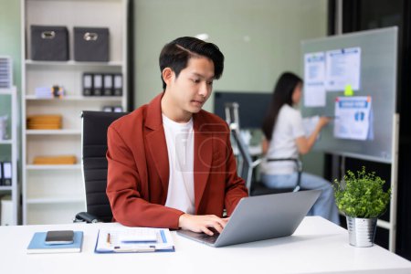 Foto de Joven atractivo asiático trabajador de oficina en trajes de negocios y el uso de ordenador portátil en la oficina - Imagen libre de derechos