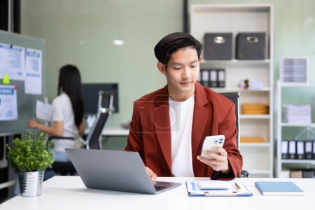 Foto de Joven atractivo asiático trabajador de oficina en trajes de negocios utilizando smartphone y computadora portátil en la oficina - Imagen libre de derechos