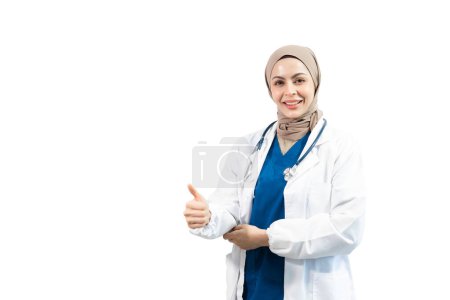Foto de Persona árabe musulmana. Médico femenino mostrando pulgares hacia arriba sobre fondo blanco aislado en estudio - Imagen libre de derechos