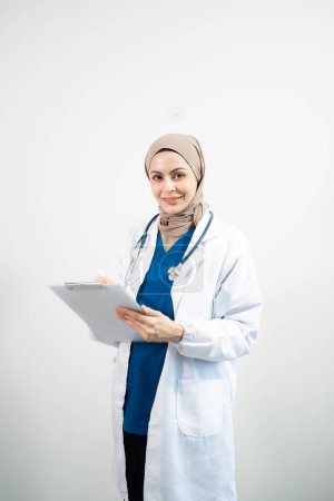 Téléchargez les photos : Arabe musulman. Le visage d'une femme médecin tenant presse-papiers dans les mains sur un fond blanc isolé en studio - en image libre de droit
