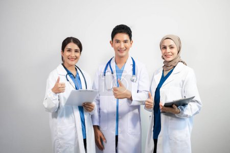 Téléchargez les photos : Équipe réussie de médecins souriants debout sur fond blanc et montrant les pouces vers le haut - en image libre de droit