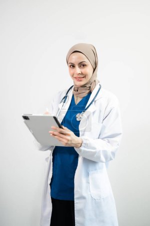 Téléchargez les photos : Arabe musulman. Le visage d'une femme médecin utilisant une tablette numérique sur fond blanc isolé en studio - en image libre de droit