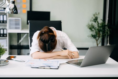 Téléchargez les photos : Femme asiatique se sentant migraine tête tendue.Femme d'affaires surmenée fatiguée après le travail au bureau et couchée sur le bureau - en image libre de droit