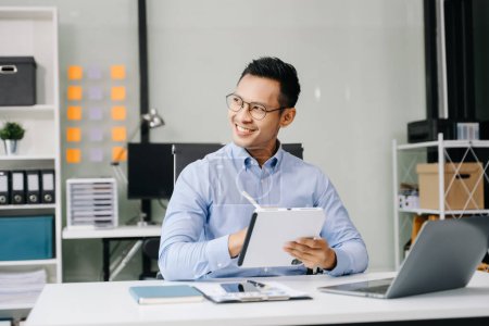 Téléchargez les photos : Asiatique homme d'affaires utilisant tablette numérique tout en étant assis sur le lieu de travail dans le bureau - en image libre de droit