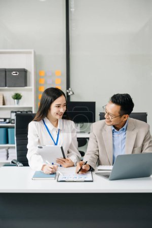 Téléchargez les photos : Deux travailleurs d'affaires asiatiques parlent pendant la réunion et utilisent un ordinateur portable au bureau - en image libre de droit