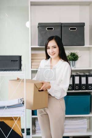 Téléchargez les photos : Femme asiatique heureuse et excitée célébrant sa démission, portant des affaires personnelles. quitter un emploi, changer ou une entreprise dans un bureau moderne - en image libre de droit