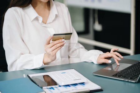 Foto de Mujer que utiliza la tarjeta de crédito y ordenador portátil para los pagos y compras en línea, mientras está sentado en la mesa en la oficina - Imagen libre de derechos