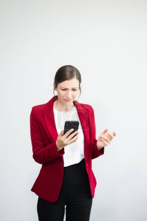 Téléchargez les photos : Femme d'affaires déçue debout sur fond blanc et utilisant un smartphone - en image libre de droit