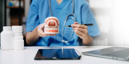 Zahnarzt sitzt am Tisch mit Kieferproben Zahnmodell und arbeitet mit Tablet und Laptop in Zahnarztpraxis professionelle Zahnklinik.
