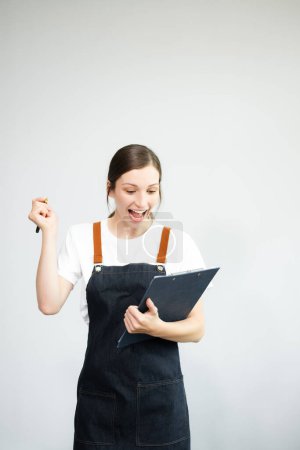 Téléchargez les photos : Caucasian woman entrepreneur in apron or shop owner making notes in the clipboard Isolated on white background - en image libre de droit