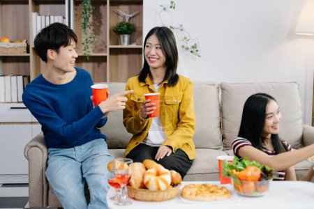 Foto de Grupo de jóvenes amigos asiáticos teniendo, disfrutar de la fiesta nocturna juntos en casa. Atractivos hombres y mujeres jóvenes divirtiéndose, disfrutando de bebidas, celebrando en el hogar moderno - Imagen libre de derechos