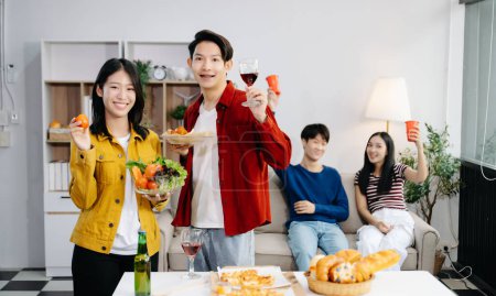 Téléchargez les photos : Groupe de jeunes amis asiatiques ayant, profiter de soirée ensemble à la maison. Jeunes hommes et femmes attrayants s'amusant, prenant des boissons, célébrant à la maison moderne - en image libre de droit