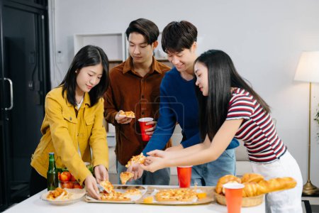 Téléchargez les photos : Groupe de jeunes amis asiatiques ayant, profiter de soirée ensemble à la maison. Jeunes hommes et femmes attrayants qui s'amusent, mangent et boivent, fêtent chez eux - en image libre de droit