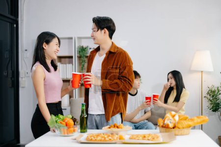 Photo for Group of Young Asian friends having, enjoy evening party together at home. Attractive young men and women having fun, enjoying drinks, celebrating at modern home - Royalty Free Image