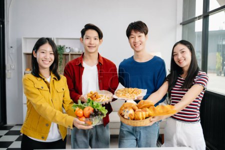 Photo for Group of Young Asian friends having, enjoy evening party together at home. Attractive young men and women holding food on the plates and celebrating at modern home - Royalty Free Image